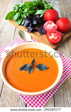 Fresh diet tomato soup with basil and raw tomatoes in ceramic bowl on wood table ready to eat