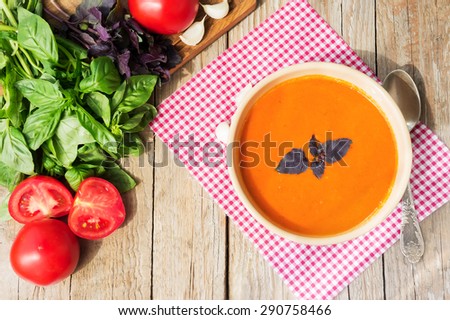 Fresh tomato soup with basil and raw tomatoes in ceramic bowl on wood table ready to eat