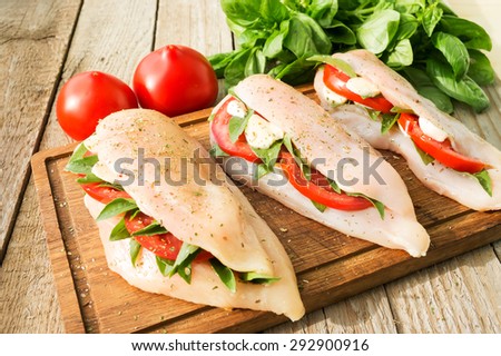 Raw chicken breasts stuffed with mozzarella, tomatoes and basil on rustic wooden table