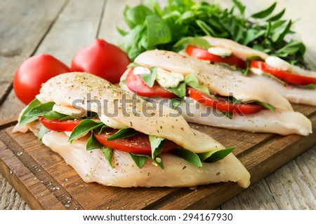 Raw chicken breasts stuffed with mozzarella, tomatoes and basil on rustic wooden table