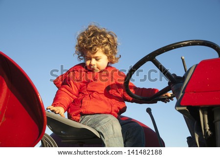 Small boy in red jacket playing on red tractor.