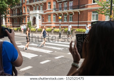 LONDON, ENGLAND - JULY 17: Tourists photograph as people walk the pedestrian crossing in famous Abbey road as tyhe beatles did in 1960\'s on Abbey Road in London July 17, 2013.