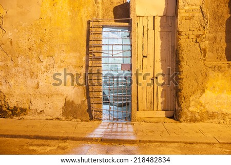 Rustic entrance, old wooden door and steel gate in a concrete and brick wall in night light, Havana, Cuba.