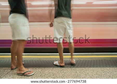 Commuters on platform, motion blur as train speeds past two men waiting for arriving train to stop.