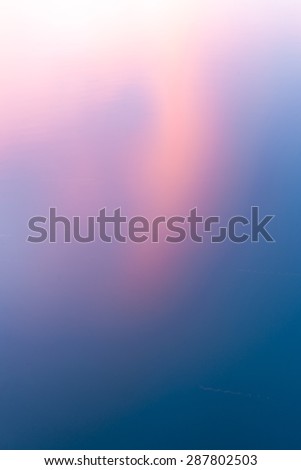 Sunset colored clouds reflecting in calm water abstract background colors transition pale pink through beep blue diagonally, vertical composition