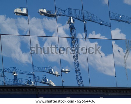 Building mirror glass wall reflecting cranes on building sites.