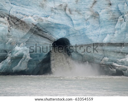 Water gushes from large hole in base of glacier face, showing environmental effects of climate warming.