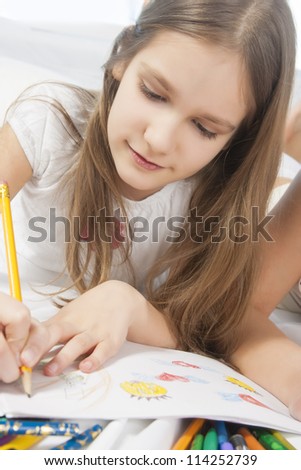 lovely portrait of a blond little caucasian girl drawing with color pencils and smiling