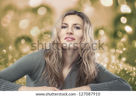 Beauty fashion portrait of young blond woman sitting against artistic background