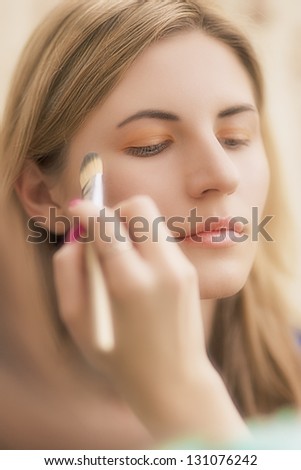 young blond woman doing makeup using makeup brush. shallow depth of field