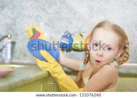 little blond girl makes dishes cleaning using water and sponge shot in household environment