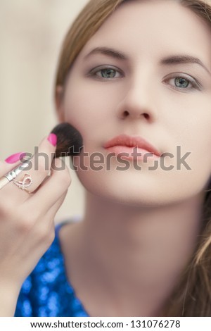young blond woman while doing makeup using makeup brush. shallow depth of field