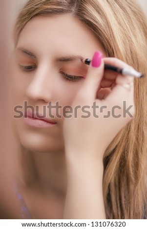 young woman is being applied makeup powder using makeup brush with her eyes closed. shallow depth of field