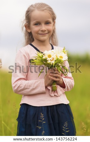 natural portrait of young cute little girl standing outside with flowers bunch