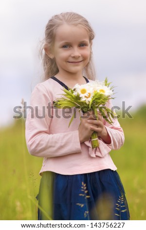 natural portrait of young cute little girl standing outside with flowers bunch