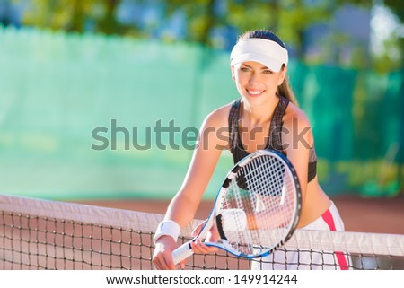Portrait of positive looking female tennis athlete with racquet standing at clay court. horizontal image