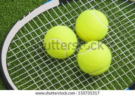 Three tennis balls lie on a tennis racket strings. over green lawn surface. tennis concept.horizontal image