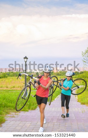 Portrait of Young Caucasian Sportswomen Work Out with Bicycle Outside. Vertical Image Orientation