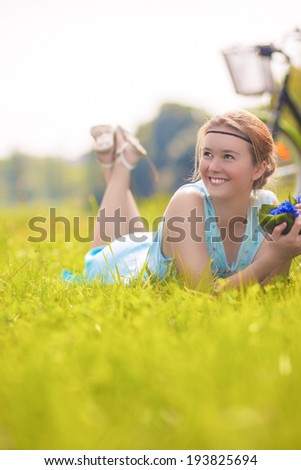Young Charming Smiling Light-Haired Woman Lies on Green Grass in Summer Park with Flowers Bouquet. Vertical Image