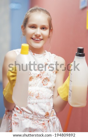 Portrait of Playful Teenage Blond Girl Holding Cleaning Tools in the Kitchen. Vertical Image