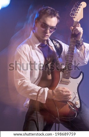 Portrait of Male Guitarist Playing with Expression. Shot with Strobes and Halogen Light on Slow Shutter Speed. Mixture of Flash and halogen Lights. Vertical Image