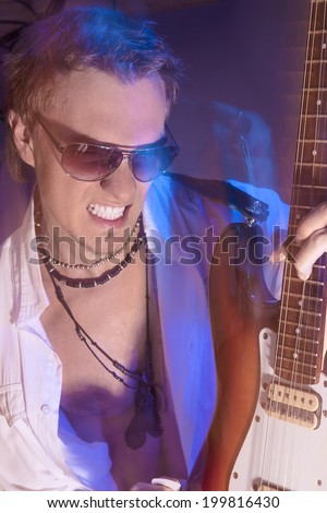 Passionate Guitarist Playing with Expression. Shot with Strobes and Halogen Light on Slow Shutter Speed To Create Mood. Mixture of Flash and Halogen Lights. Vertical Image