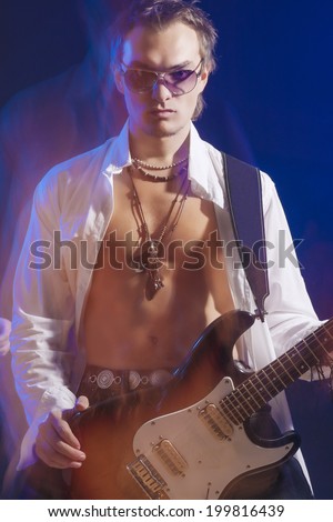Male Guitarist Posing With Guitar. Shot with Strobes and Halogen Light on Slow Shutter Speed. Mixture of Flash and halogen Lights. Vertical Image