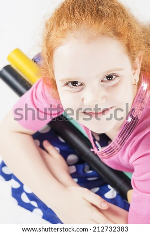 Cute and Happy Red-haired Caucasain Girl Holding Long and Big Pencils. Posing Against White Background. Vertical Image
