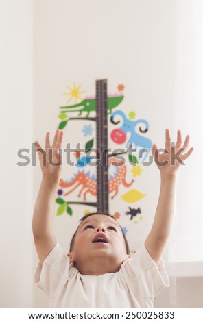 Portrait of Little Caucasian Boy Using Wall Ruler for Making Height Measurements. Vertical Shot