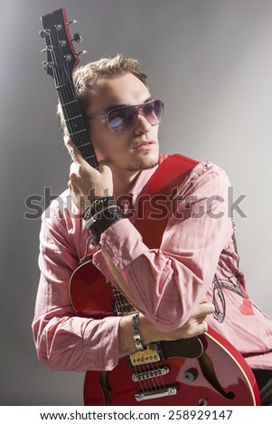 Portrait of Thoughtful Caucasian Guitar Player with Stylish Guitar Standing Against Gray Background. Vertical Image Orientation