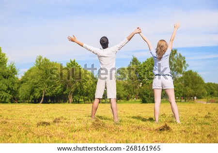 Young Caucasian Couple Standing Together on Grass Meadow with hands Lifted Up. Horizontal Image