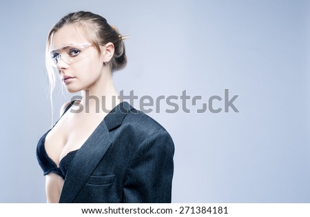 Portrait of Sexy Sensual Caucasian Blond Model Dressed in Grey Modern Suite and Posing in Transparent Glasses Against Gray Background. Horizontal Image Concept