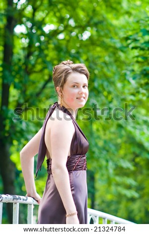young charming lady with curly fashion hair dressing and silk skin standing on the bridge body turned left head turned right smiling in sever violet dress