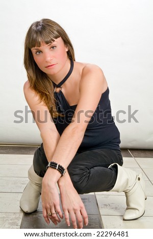 young lady sitting with legs crossed hands crossed appear put forward on knees in black jeans and black blouse  on white background