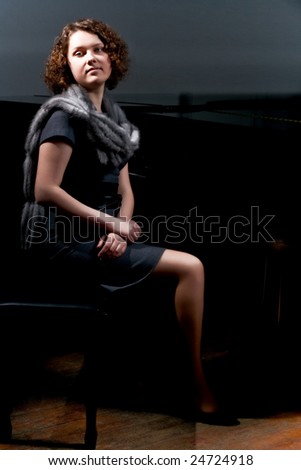 pretty young lady sitting near black piano in grey dress with fur scarf around neck isolated