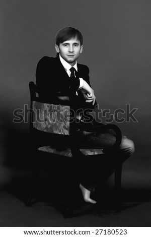blonde man sitting on old chair turned back looking forward,wearing  jeans,white shirt,black tie,jacket,with hands free pose appear and legs free isolated