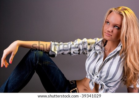 young sensual blonde woman sitting dreaming in blue jeans and striped modern shirt isolated over gray