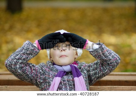 young pretty girl having fun siting in the autumn park with lifted hands near face