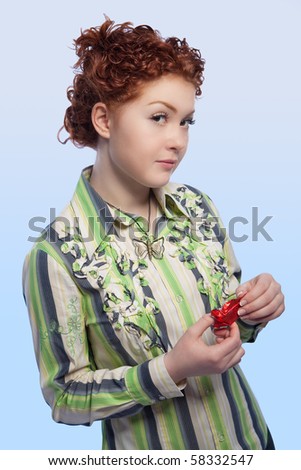 calm and beautiful young red haired girl with curly natural hair unwraping chokolate candy bar standing with curious facial expression and isolated over light blue background