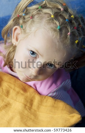 little cute blond caucasian girl looking up with calm sincere look from behind a pillow having long hair tails on head