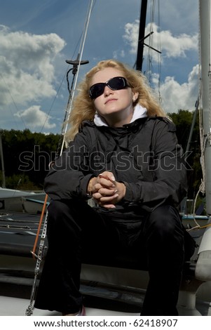 young caucasian blond girl sitting on yacht board wearing black sunglasses and water-proof clothes. this image was made with flash strobe on location.