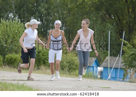 three young running girlfriends on the road smiling and holding hands together and having fun