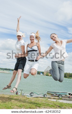 three caucasian nice and beautiful young girls holding hands together and jumping out on  the hill over water background