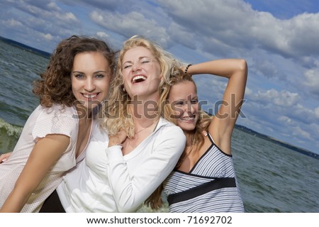 three young nice caucasian sporty ladies having fun outside and resting near seaside shore  close together and smiling happily