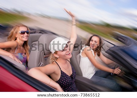 three happy and sensual caucasian girlfriends having drive on a red cabriolet car with bright positive expressions. shoot made on location with strobes