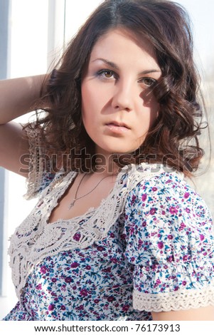 seriously looking young caucasian girl standing with lifted hand in front of the big window with passionate expression