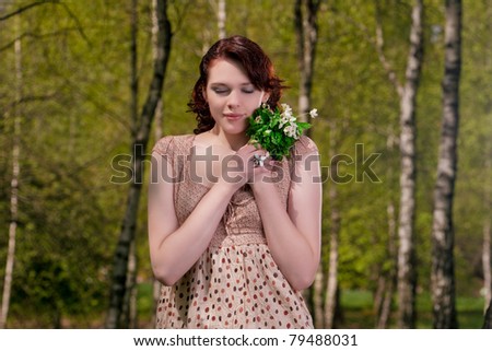 young and pretty caucasian brunette girl standing outside in green forest and holding bunch of flowers outside. shot made with strobes on location