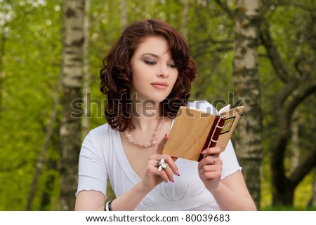 happy young caucasian brunette girl with book in spring forest reading