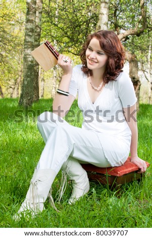 brunette girl in spring forest with little book in hands sitting on chair - shot outside