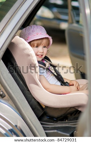 little cute girl in cap sitting in the car in child safety seat and smiling